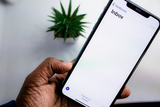 A close-up view of a smartphone screen displaying the email inbox, held by an adult's hand.